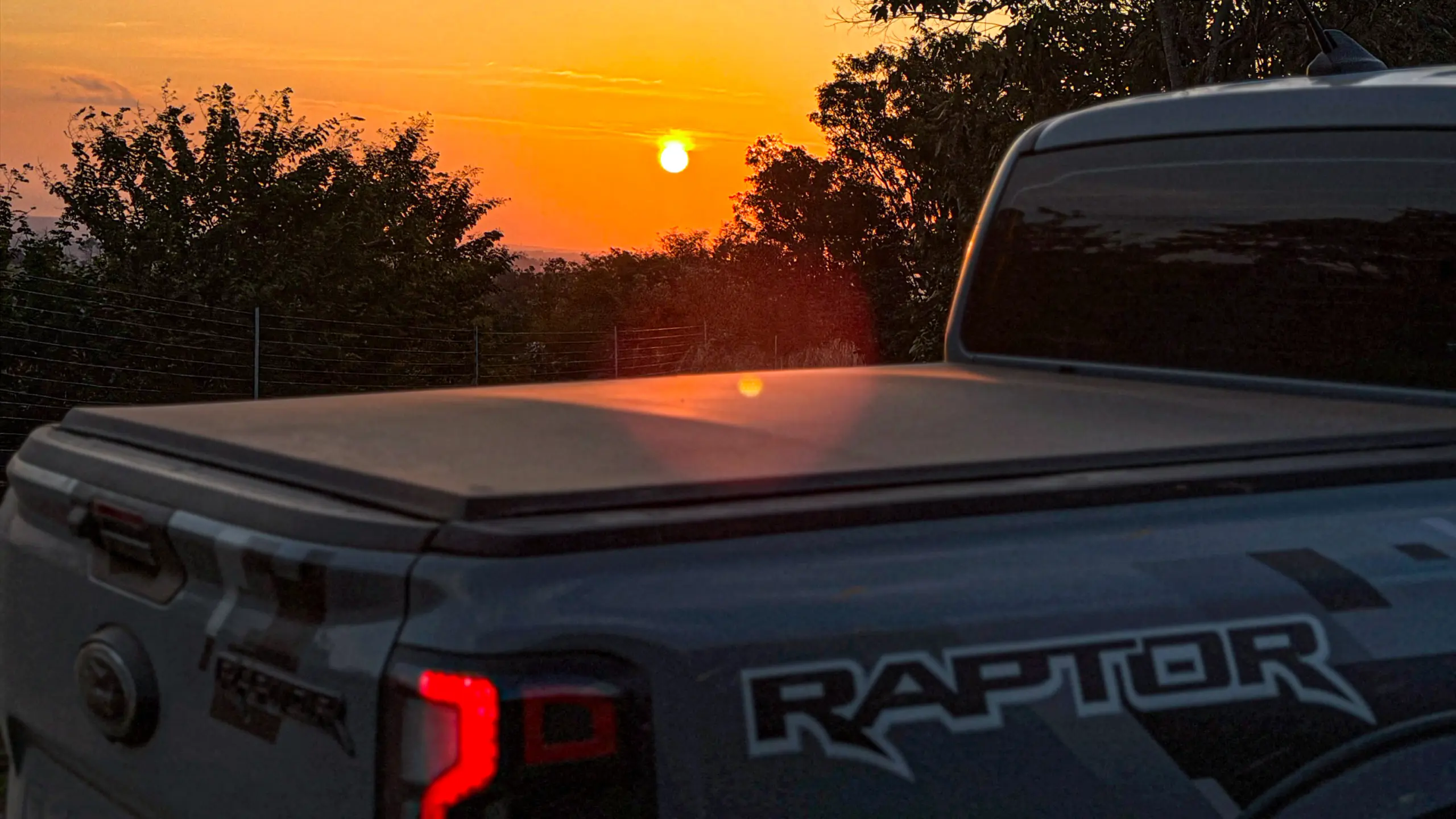 Ford Ranger Raptor suja de barro e terra estática na grama na cor Cinza Interlagos com pôr do sol
