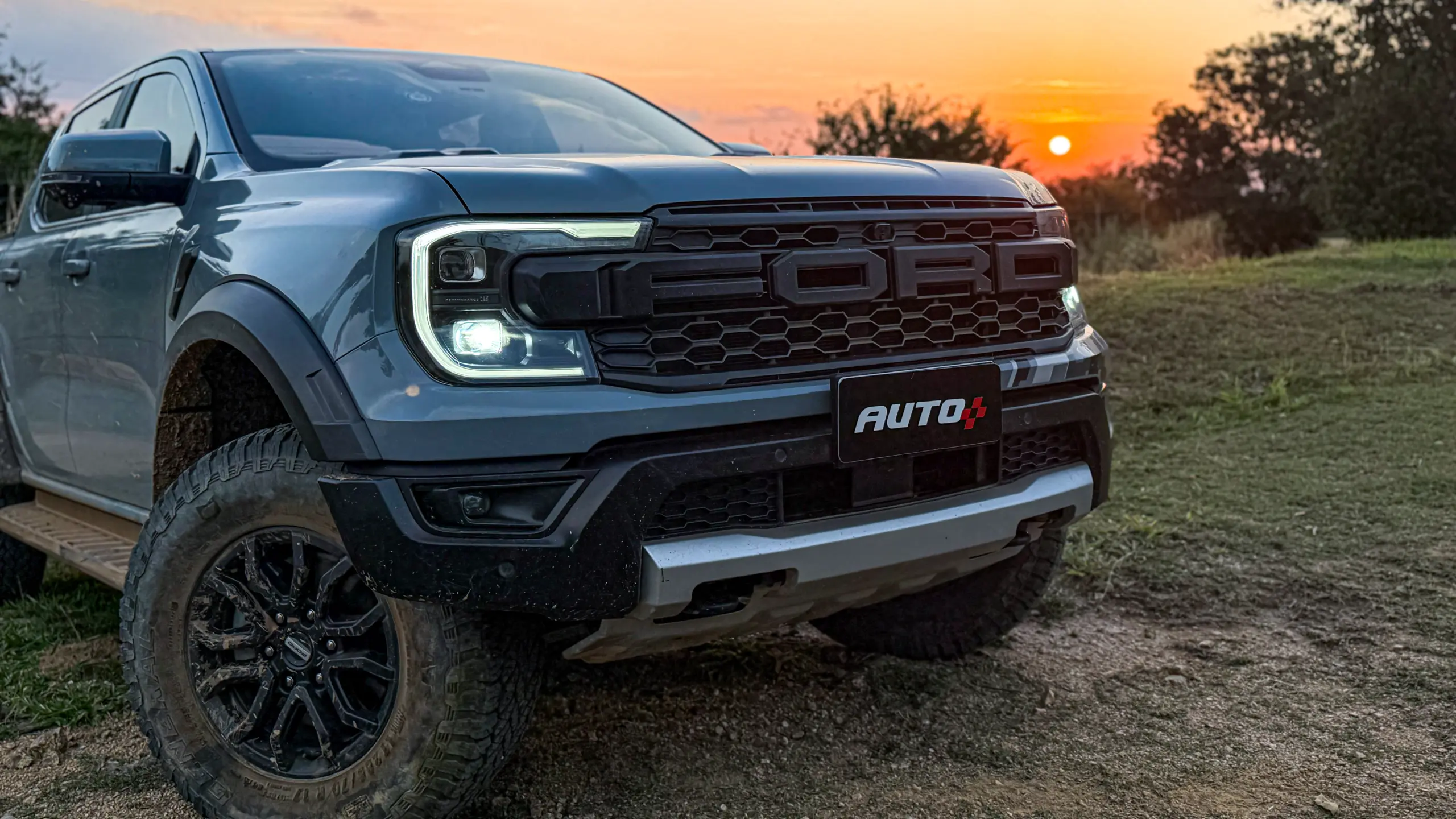 Ford Ranger Raptor suja de barro e terra estática na grama na cor Cinza Interlagos com pôr do sol