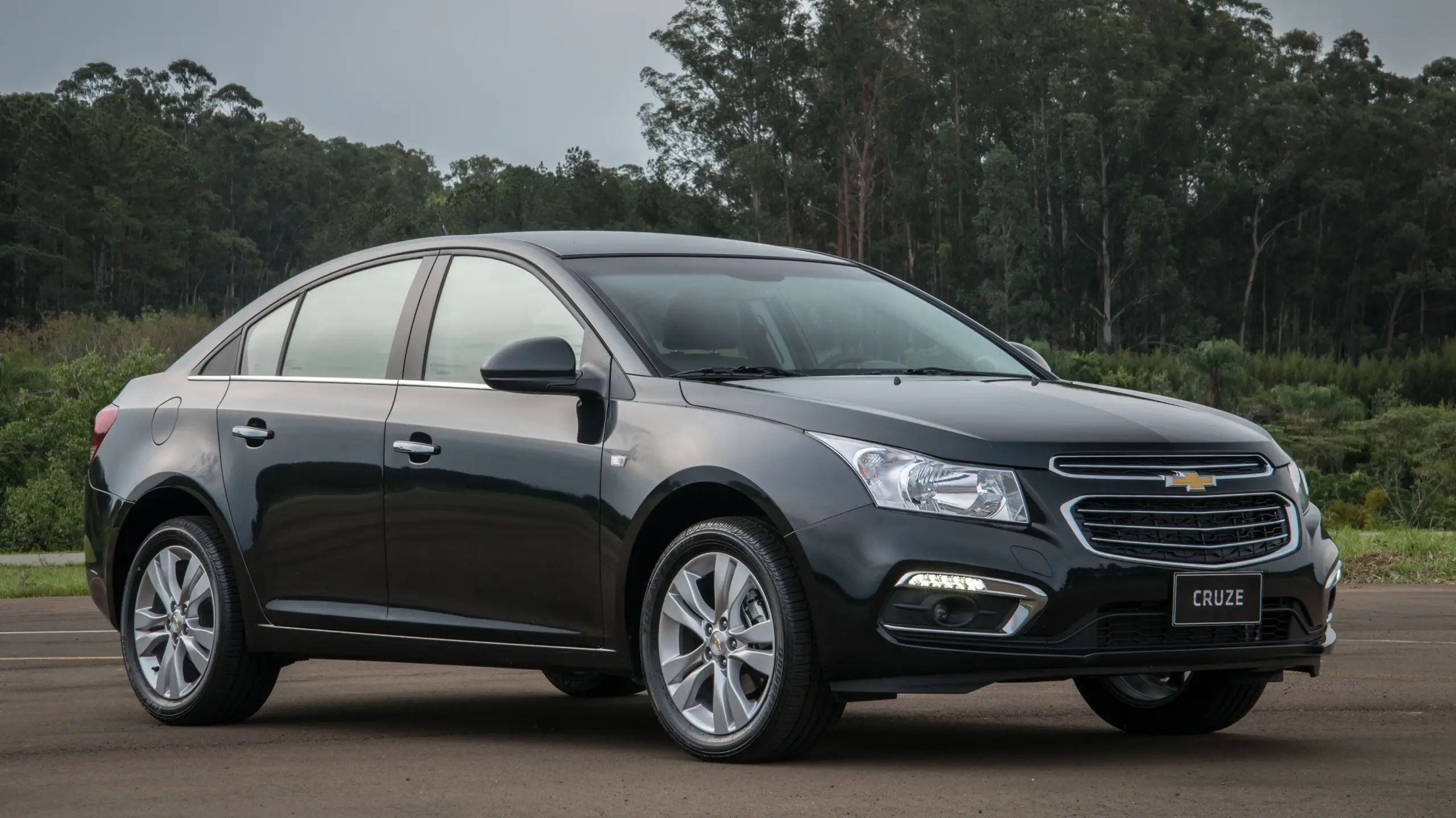 Chevrolet Cruze Sedan preto, visto de frente e com mato ao fundo
