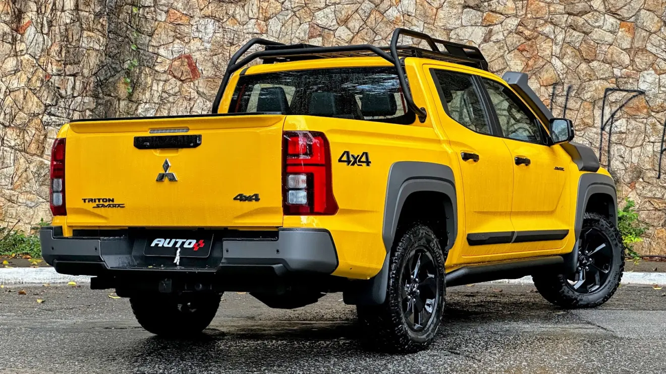 Mitsubishi Triton Savana amarela parada de traseira com muro de pedras ao fundo 