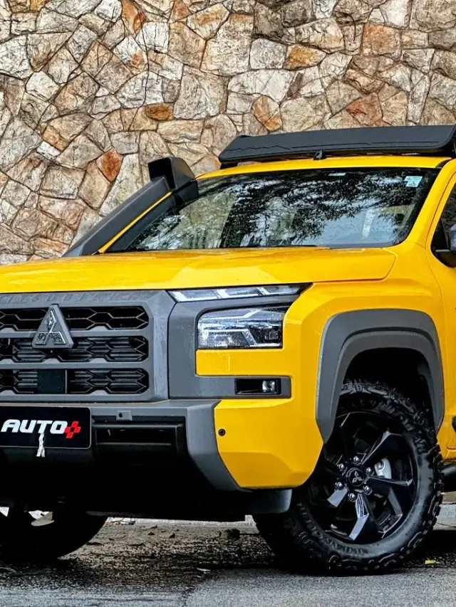 Caminhonete Mitsubishi Triton Savana amarela parada de frente com muro de pedras ao fundo