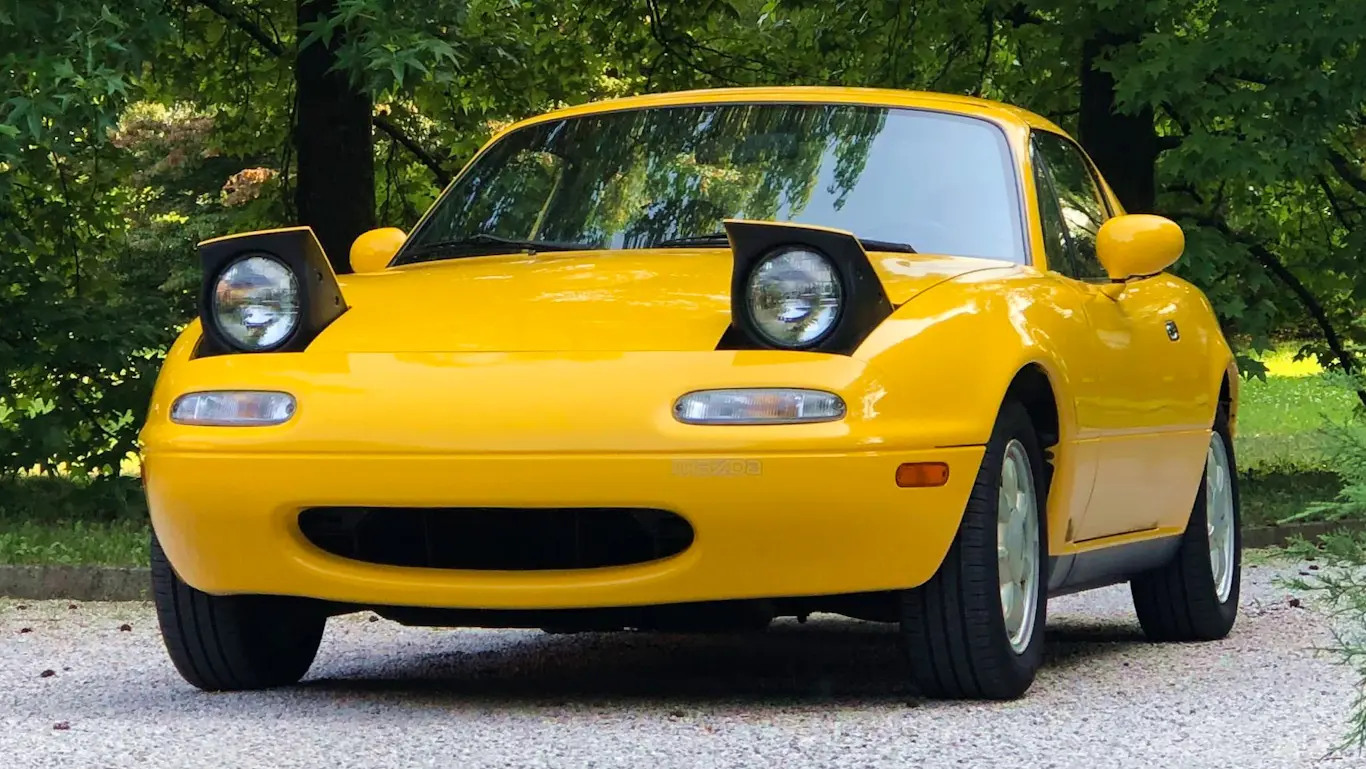 Equipamentos. Mazda Miata amarelo de primeira geração parado de frente