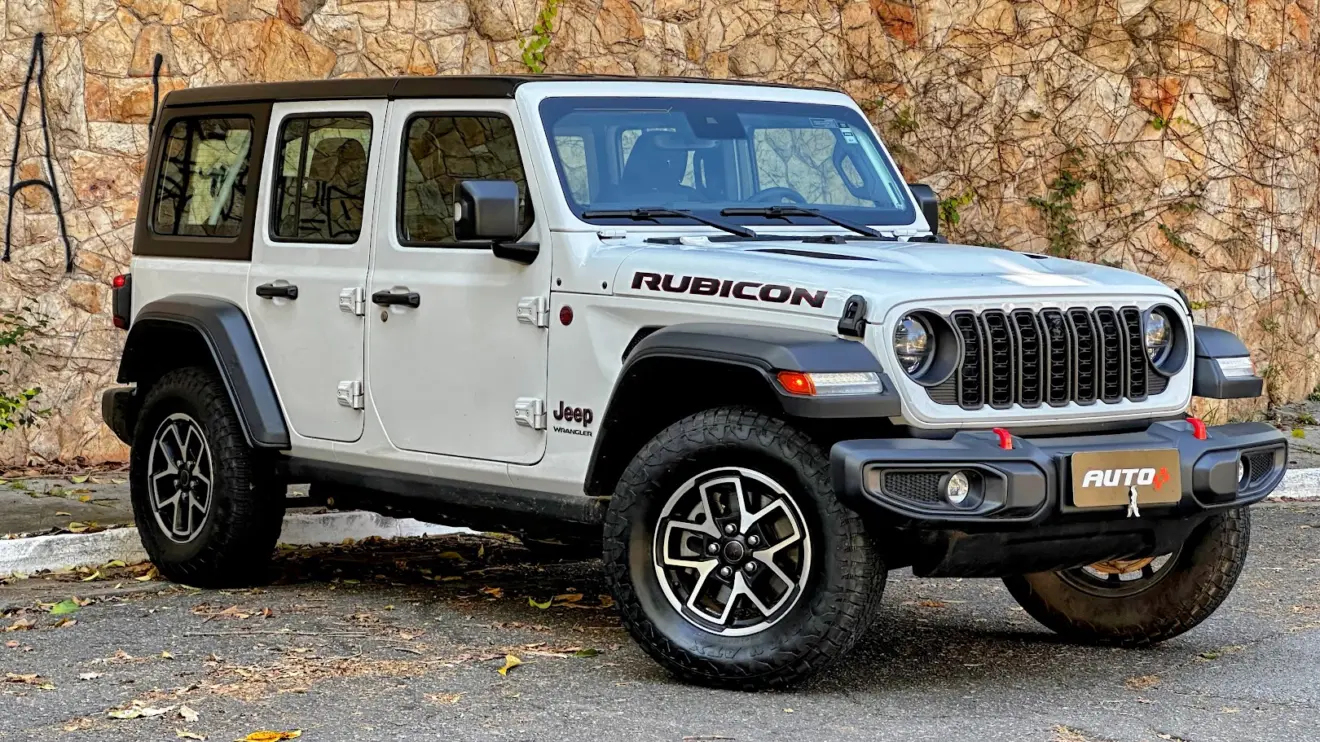 Jeep Wrangler Rubicon 4x4 branco parado de frente com muro de pedras ao fundo