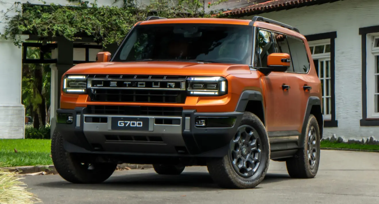 Jetour G700 laranja fosco parado de frente com casa ao fundo