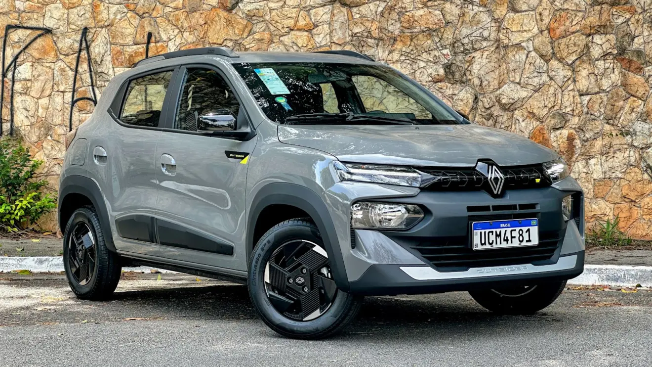 Renault Kwid Outsider cinza parado de frente com muro de pedras ao fundo