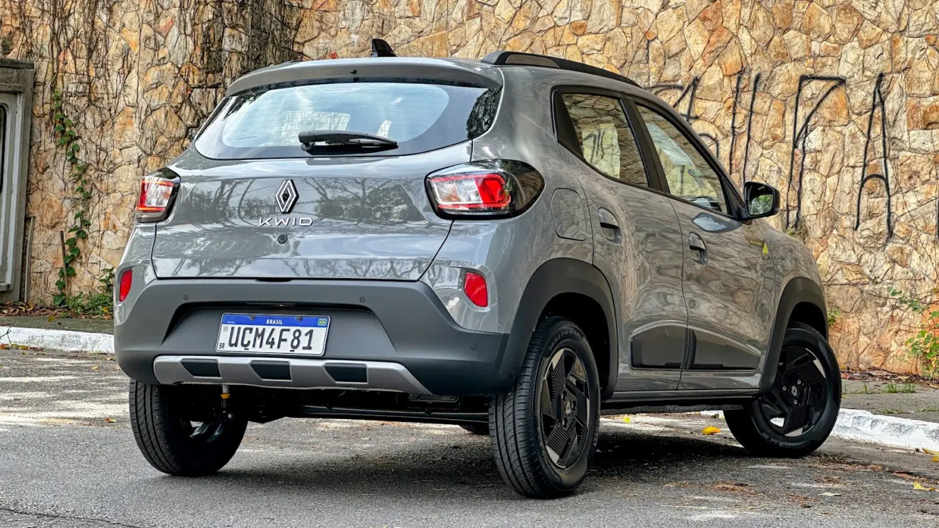 Renault Kwid Outsider cinza parado de traseira com muro de pedras ao fundo